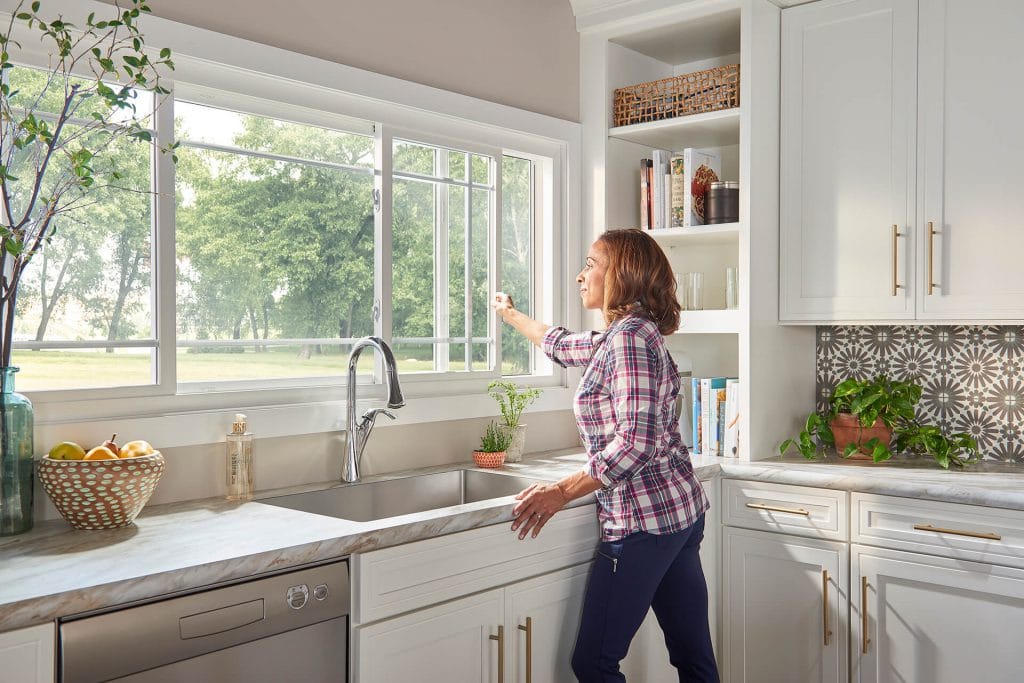 Woman opens awning window in kitchen.